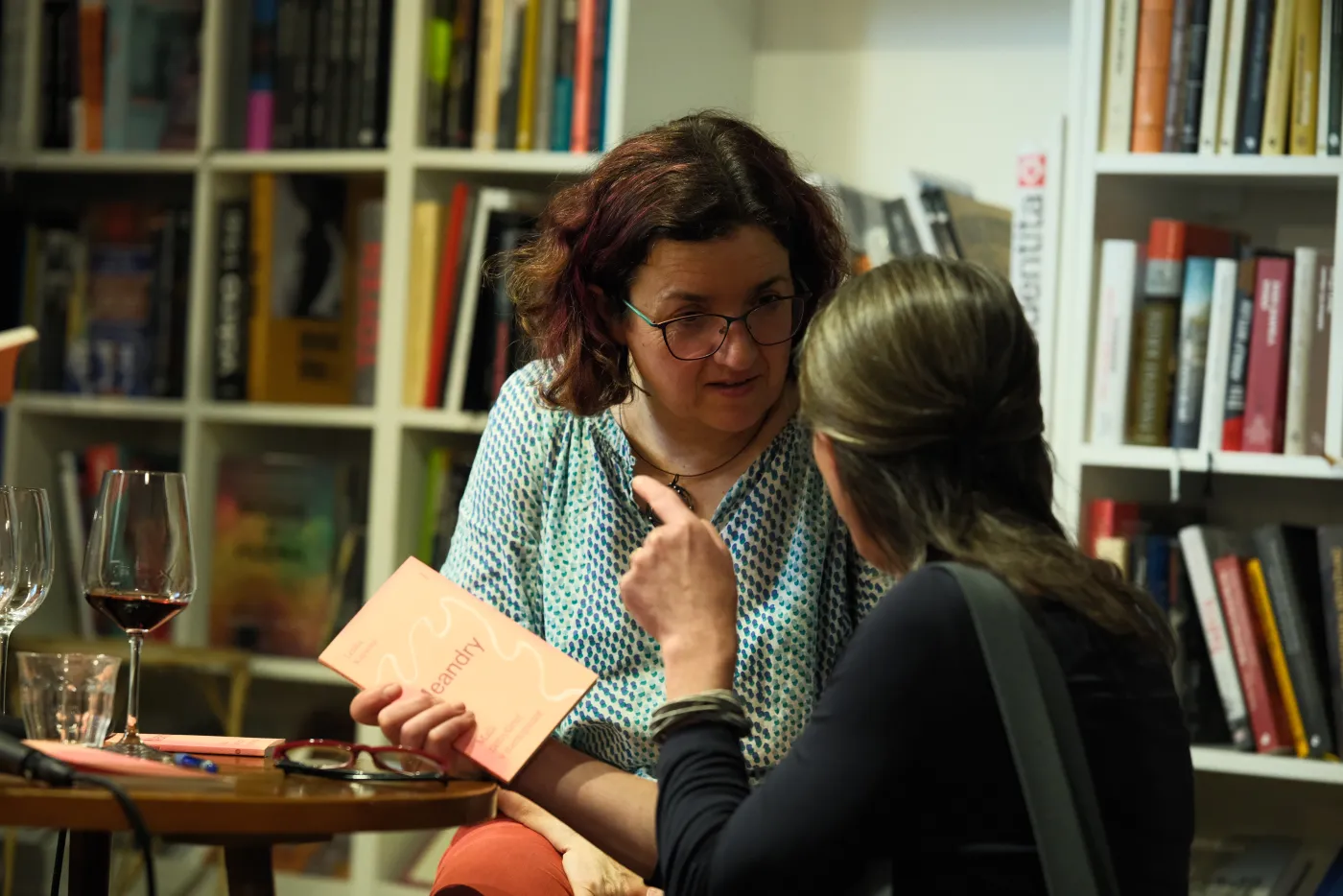 Lenka Kapsová ukazuje knihu Meandry čtenářce u stolku